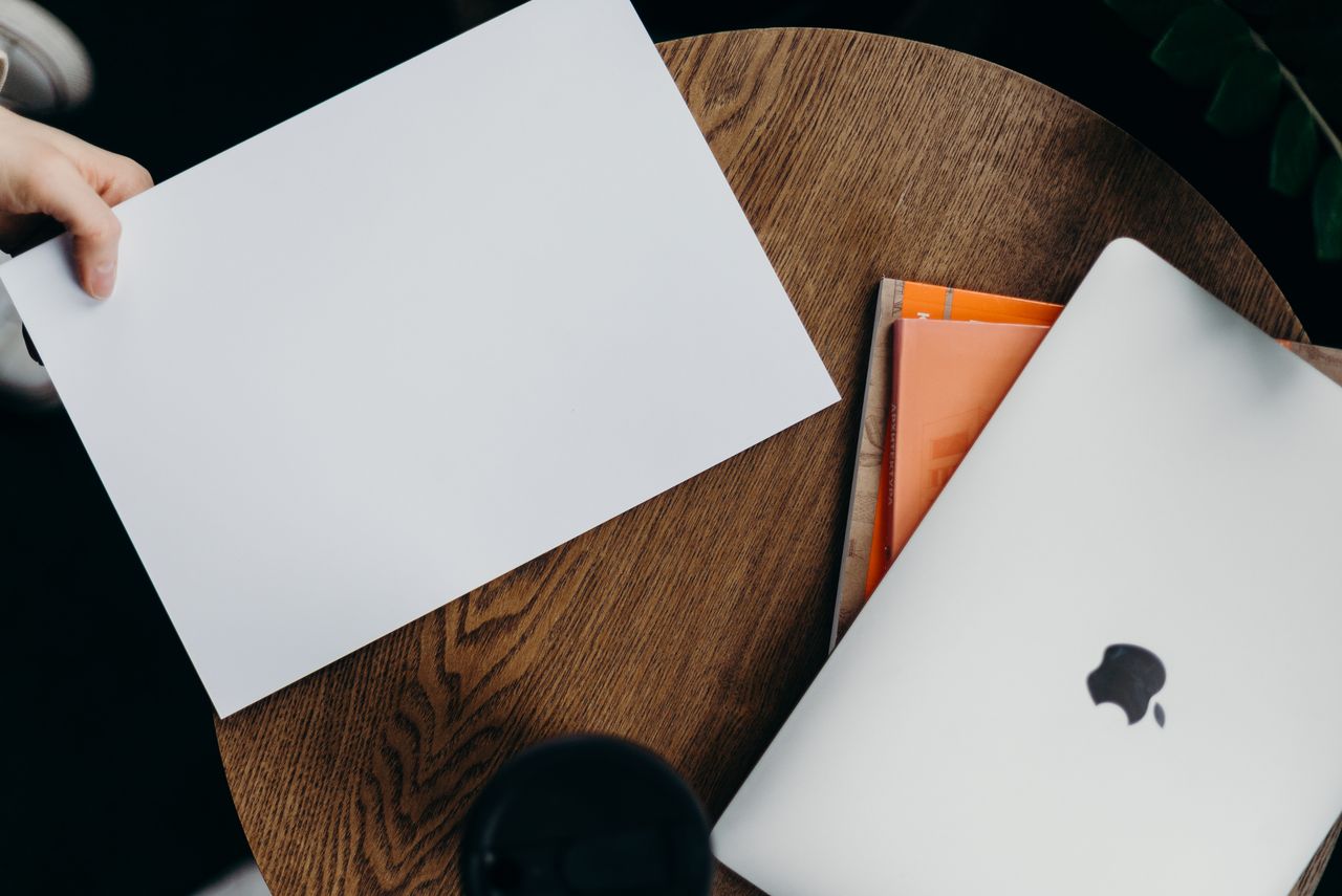 Vue plongeante d’un espace de travail épuré avec un ordinateur portable et une feuille blanche posés sur une table en bois.